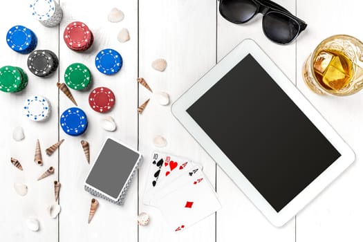 Gambling. Poker chips, cards and the dice nearby tablet on white wooden table. Top view. Copyspace. Poker. Summer