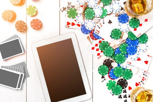 Gambling. Poker chips, cards and the dice nearby tablet on white wooden table. Top view. Copyspace. Poker. Summer. Sun flare