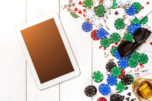 Gambling. Poker chips, cards and the dice nearby tablet on white wooden table. Top view. Copyspace. Poker. Summer. Sun flare