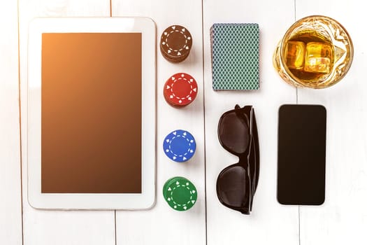 Gambling. Poker chips, cards and the dice nearby tablet on white wooden table. Top view. Copyspace. Poker. Summer. Sun flare