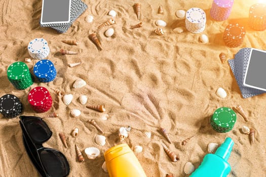 Gambling on vacation concept - white sand with seashells , colored poker chips and cards. Top view. Copy space. Summer. Sun flare