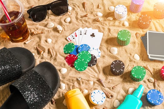 Gambling on vacation concept - white sand with seashells , colored poker chips and cards. Top view. Copy space. Summer. Sun flare