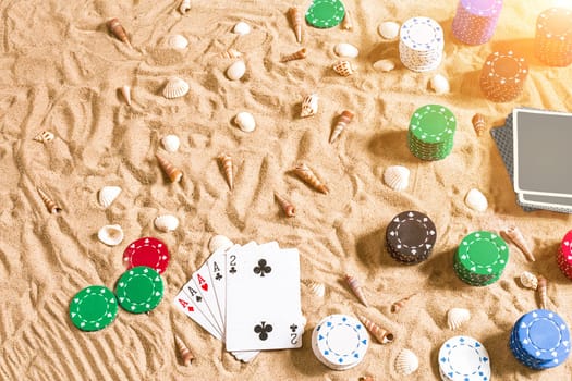 Gambling on vacation concept - white sand with seashells , colored poker chips and cards. Top view. Copy space. Summer. Sun flare