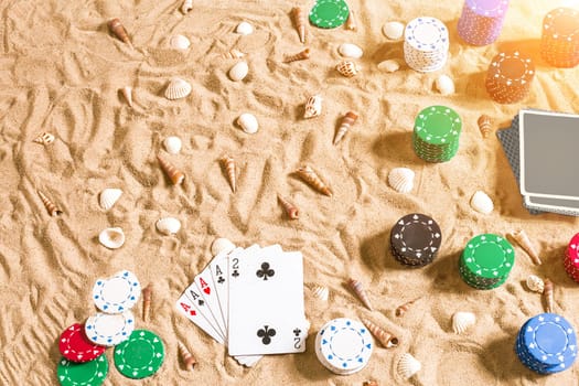 Gambling on vacation concept - white sand with seashells , colored poker chips and cards. Top view. Copy space. Summer. Sun flare