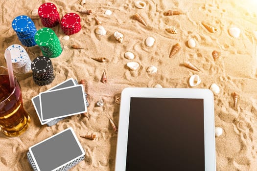 Online poker game on the beach with digital tablet and stacks of chips. Top view. Copy space. Flat lay. Sun flare