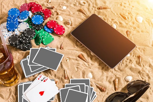 Gambling on vacation concept - white sand with seashells , colored poker chips and cards. Top view. Copy space. Summer. Sun flare