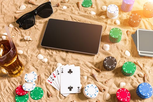 Online poker game on the beach with digital tablet and stacks of chips. Top view. Copy space. Flat lay. Sun flare