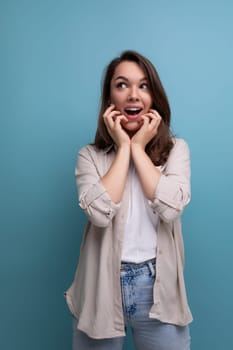 surprised emotional brunette 30 year old female person dressed in a shirt and jeans looks away on a blue background.