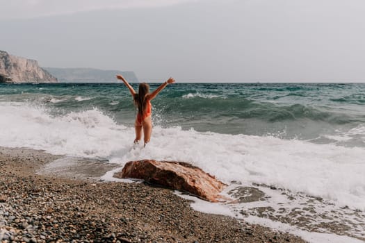 Woman travel sea. Young Happy woman in a long red dress posing on a beach near the sea on background of volcanic rocks, like in Iceland, sharing travel adventure journey