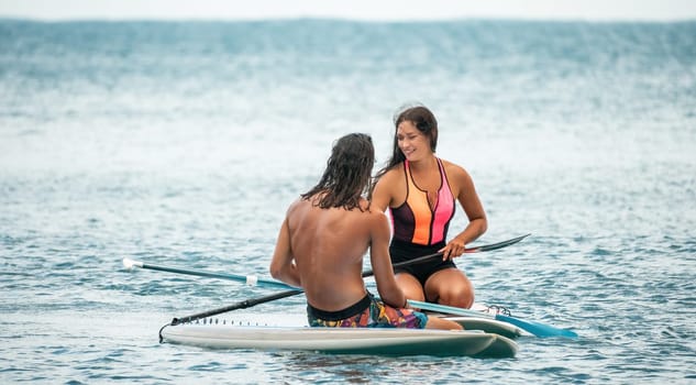 Sea woman and man on sup. Silhouette of happy young woman and man, surfing on SUP board, confident paddling through water surface. Idyllic sunset. Active lifestyle at sea or river