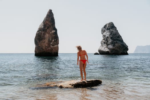 Woman travel sea. Young Happy woman in a long red dress posing on a beach near the sea on background of volcanic rocks, like in Iceland, sharing travel adventure journey