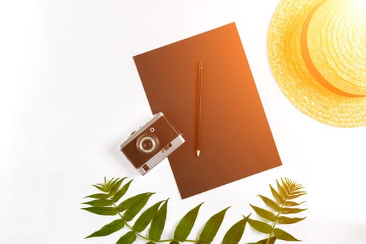 Straw hat with green leaves and old camera on white background, Summer background. Top view. Copy space. Still life. Flat lay. Sun flare