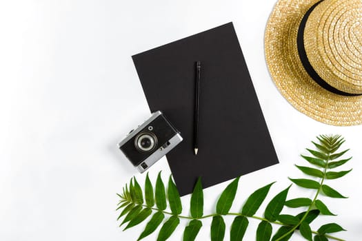 Straw hat with green leaves and old camera on white background, Summer background. Top view. Copy space. Still life. Flat lay