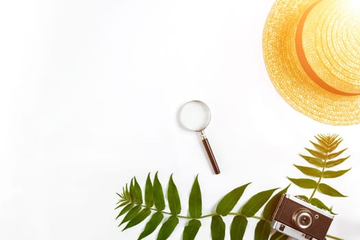 Straw hat with green leaves and old camera on white background, Summer background. Top view. Copy space. Still life. Flat lay. Sun flare