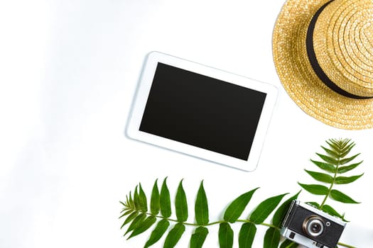 Straw hat with green leaves, tablet and old camera on white background, Summer background. Top view. Copy space. Still life. Flat lay