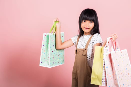 Asian little kid 10 years old smiling holding multicolor shopping bags in hands at studio shot isolated on pink background, Portrait of Happy child girl shopper lifestyle, Black friday concept