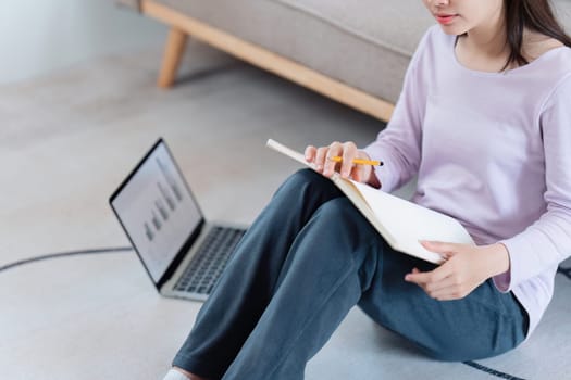 Online education, e-learning. Asian woman in stylish casual clothes, studying using a laptop, listening to online lecture, taking notes, online study at home.
