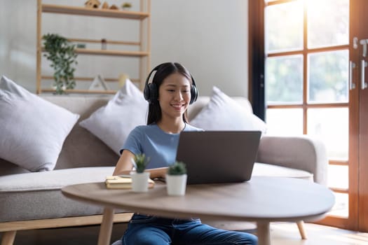 Young business freelance Asian woman working on laptop checking social media while sit on the sofa when relax in living room at home. Lifestyle at house concept.