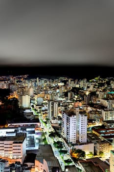 A stunning view of a city at night with skyscrapers and buildings illuminated, taken with a long exposure. The cloudy sky adds a dramatic touch to the scene. Plenty of space for text.