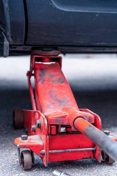 car wheel replacement. lifting the car with the help of an automobile hydraulic jack. regular maintenance of the car Orange hydraulic jack for floor repair. Service. vertical photo