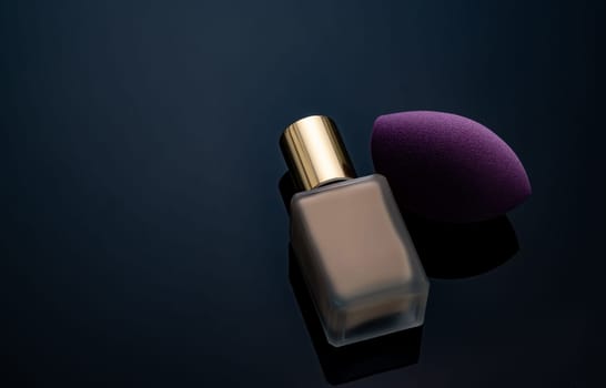 Purple makeup sponge on dark background. Soft makeup cosmetic sponge. Flat-ended makeup sponge with blur makeup foundation bottle. Liquid beige make-up foundation and beauty blender. Cosmetic product.