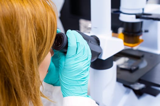 A woman scientist is performing biological analysis while observing samples through a microscope.