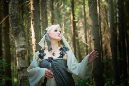 Adult mature woman 40-60 in a green long fairy dress in forest. Photo shoot in style of dryad and queen of nature. Fairy in beautiful green summer forest. Concept of caring for nature