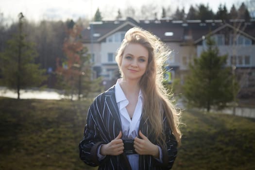 Portrait of Beautiful girl with long blonde hair in white shirt and jacket in village or small town. High young slender woman in an autumn, spring, summer day