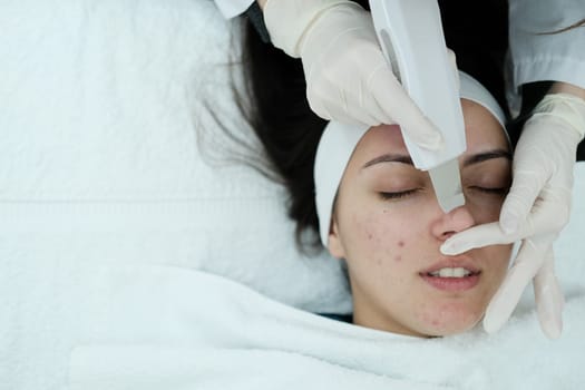 Cosmetologist making a deep facial cleansing with skin scrubber on female patient face. Ultrasound scrubber.