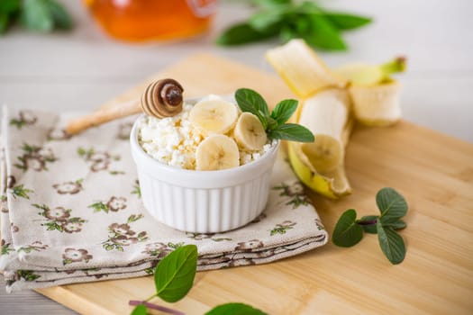 crumbly organic cottage cheese with honey and bananas in a ceramic bowl on the table