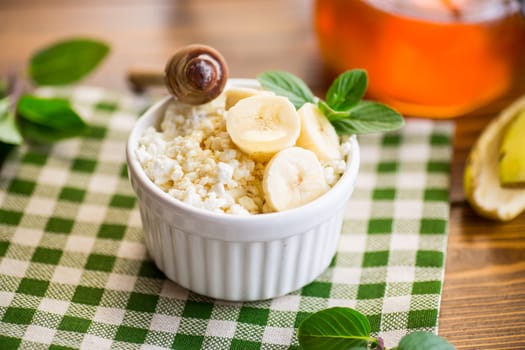 crumbly organic cottage cheese with honey and bananas in a ceramic bowl on the table