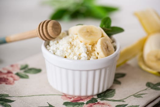 crumbly organic cottage cheese with honey and bananas in a ceramic bowl on the table