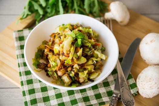 cabbage early fried with mushrooms, carrots and vegetables in a white bowl on a wooden table