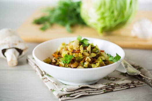 cabbage early fried with mushrooms, carrots and vegetables in a white bowl on a wooden table