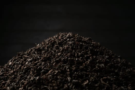 A pile of black fanning or broken loose leaf tea on a dark black background. Close-up, side view