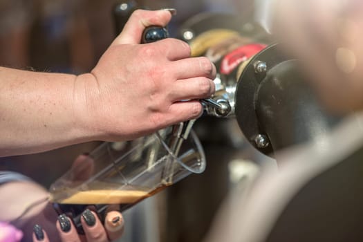 The bartender pours craft beer from the tap into a glass. The hand at the beer tap pours draft beer into a glass at the bar