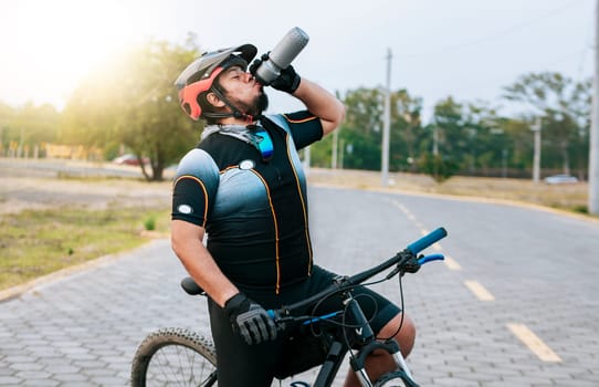 Tired cyclist drinking water outdoors. Chubby cyclist on his bike drinking water, Thirsty cyclist on his bike drinking water outside.