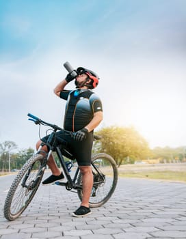 Thirsty cyclist on his bike drinking water outside. Tired cyclist drinking water outdoors, Chubby cyclist on his bike drinking water