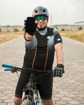 Smiling cyclist showing an advertisement on cell phone, Cyclist in sportswear showing the phone screen. Male cyclist on the bike showing cell phone screen outdoors