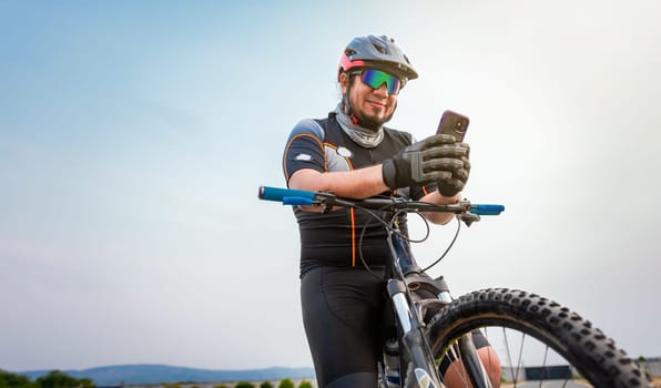 Male cyclist with helmet using cell phone. Cyclist on his bike texting with phone outdoors. cyclist man with helmet and glasses texting on cell phone outdoors