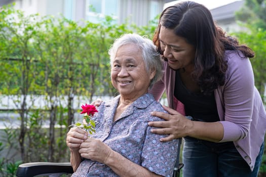 Caregver help Asian elderly woman holding red rose flower, smile and happy in the sunny garden.