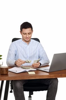 handsome freelancer man working on laptop and holding money while sitting on chair at desk.