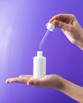 Women's hands hold pipette with cosmetic serum on lilac background,