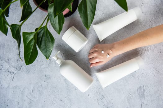 Woman apply white cream on her hands on gray background with cosmetic cream decorate with fresh green leave. Natural skincare concept.