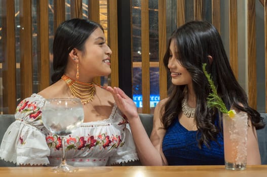 two young lesbians from different cultures on a blue sofa in a restaurant showing affection and looking at the jewelry. High quality photo