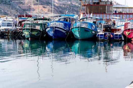 Yachts sea port. Reflection in the sea surface of multicolored yachts parked in the port on the shore. Fragment of a ship on the water and the reflection of ships in the sea. motionless mirrored water of the sea.