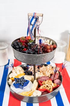 July 4th charcuterie board on a two-tiered serving metal stand filled with cheese, crackers, salami, and fresh fruits