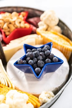 July 4th charcuterie board on a two-tiered serving metal stand filled with cheese, crackers, salami, and fresh fruits