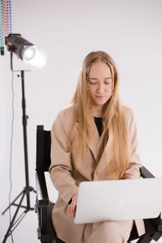 A business woman in a suit is working, typing on a laptop apple and sitting on a producer chair. portrait blonde assistant of hands with computer MacBook . Vertical