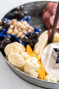 July 4th charcuterie board on a two-tiered serving metal stand filled with cheese, crackers, salami, and fresh fruits